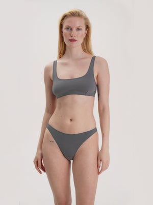 Woman wearing a gray top and bikini set on a plain background