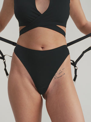 Person wearing black lingerie and strap suspender belt with stockings on a plain background