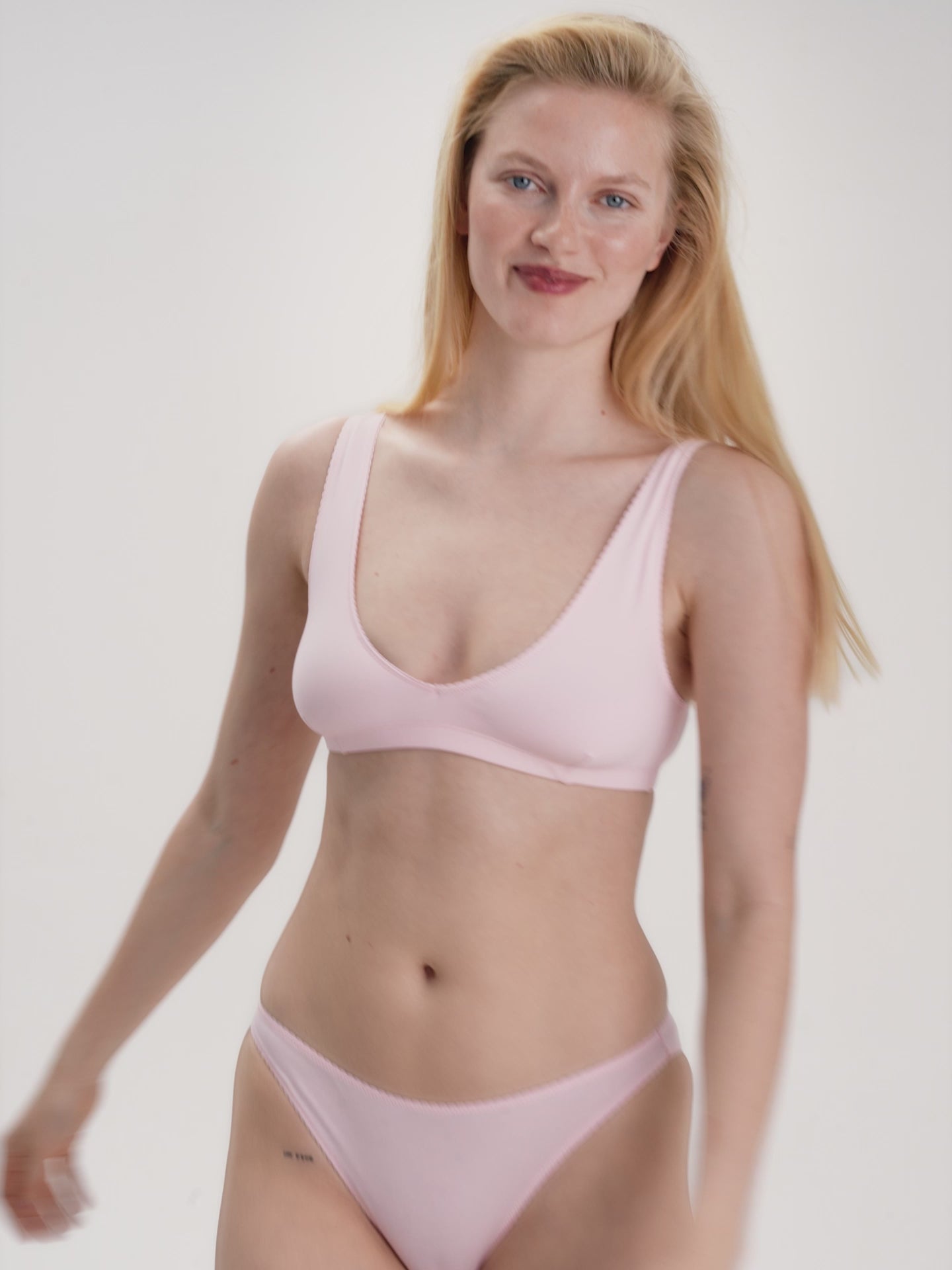 Woman wearing a light pink bralette and bikini set on a plain background