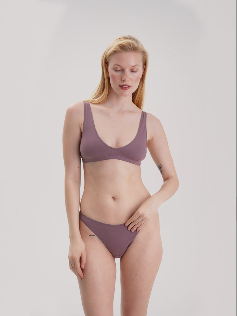 Woman wearing a mauve bralette and bikini set against a plain background