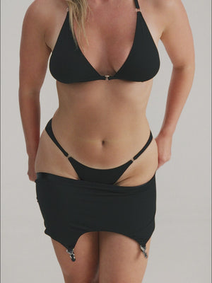 Woman wearing black lingerie set and putting on suspender belt with stockings