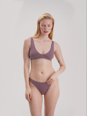 Woman wearing a mauve bralette and bikini set against a plain background