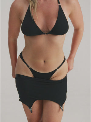 Woman wearing black lingerie set and putting on suspender belt with stockings