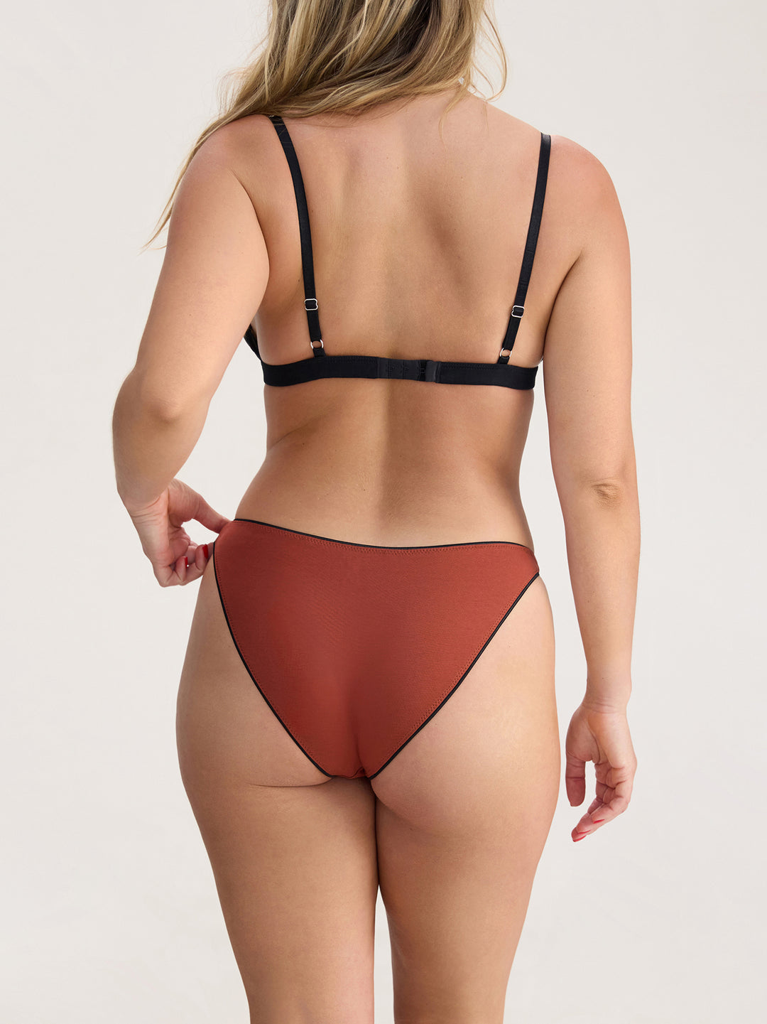 Person wearing a black bra and terracotta underwear set on a plain background